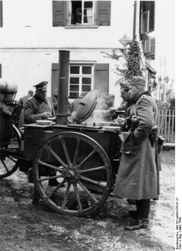 Quelle: https://upload.wikimedia.org/wikipedia/commons/8/84/Bundesarchiv_Bild_201-MA34-370-91-21%2C_Hayingen%2C_Soldaten_an_Feldk%C3%BCche.jpg